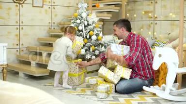 <strong>带</strong>着<strong>爸爸</strong>的幼儿在家里把礼物盒放在装饰好的圣诞树下